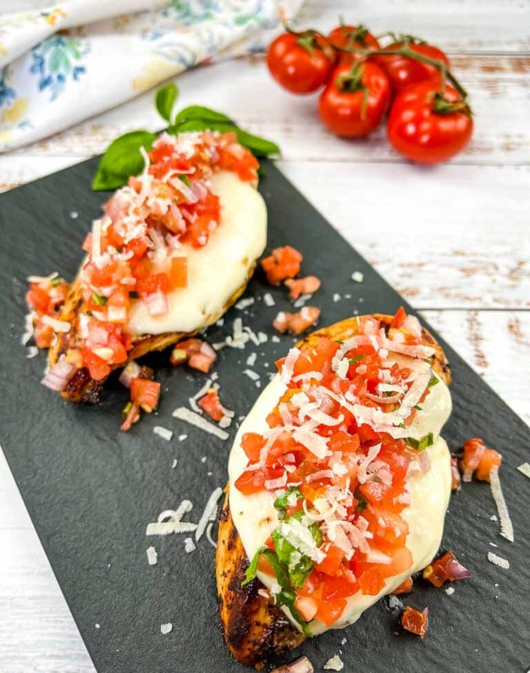 Grilled Bruschetta Chicken on a black platter with tomatoes in the background.