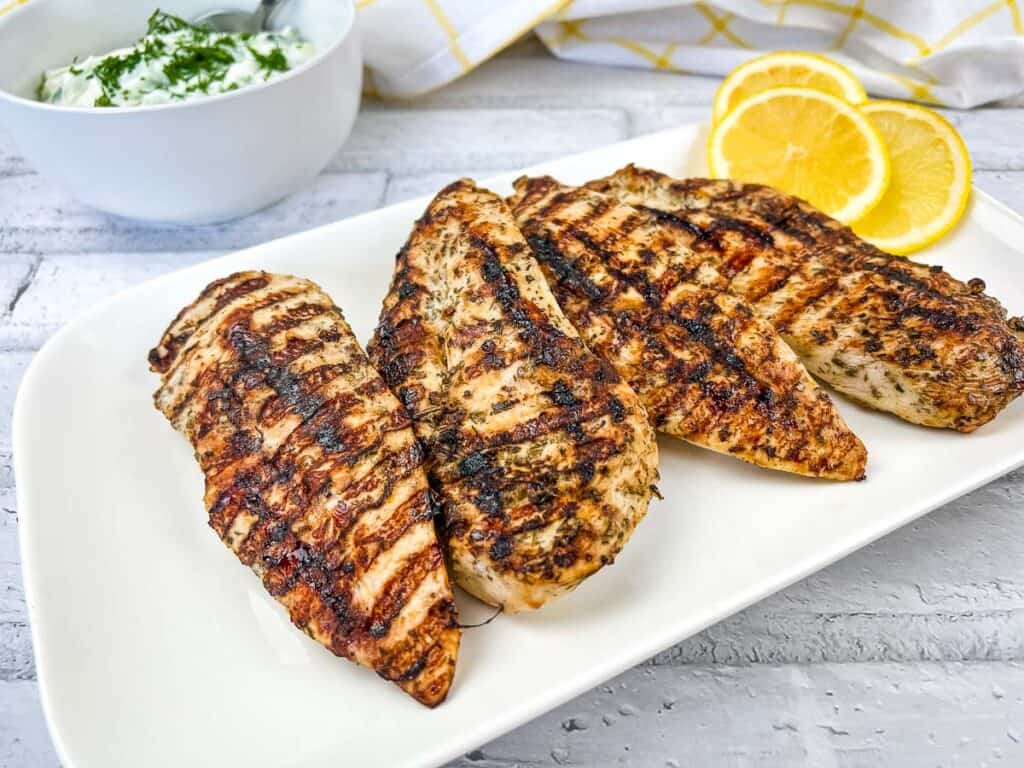 Ninja Woodfire Grilled Greek Chicken Breasts on a white platter with tzatziki in the background.