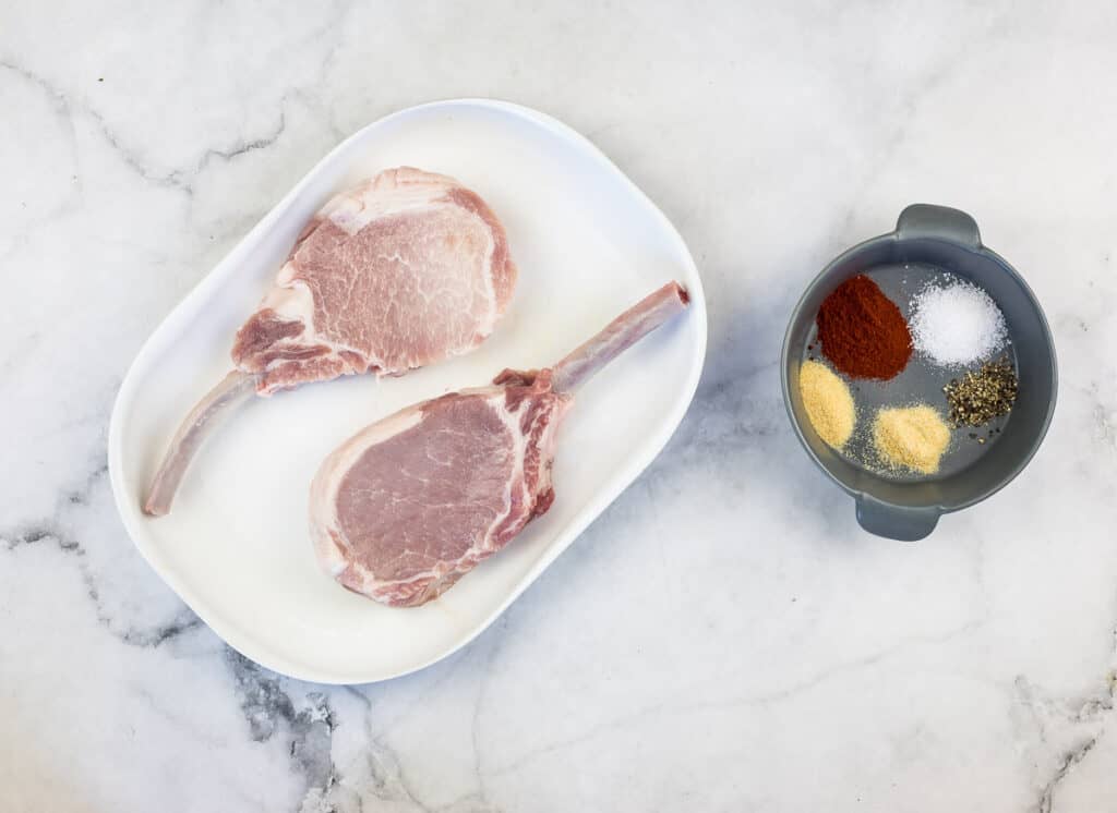 Chops on a plate with the spices in a bowl nearby.