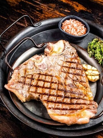 BBQ Grilled T-bone or Porterhouse beef meat Steak on a steel tray with herbs. Wooden background. Top view.