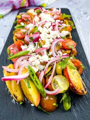 Grilled Peach Salad with Tomatoes on a black platter.