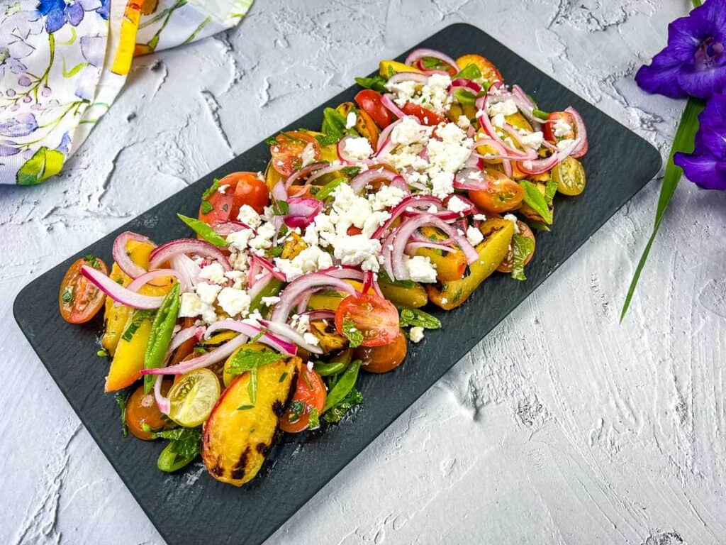 Grilled Peach Salad with Tomatoes on a black platter.