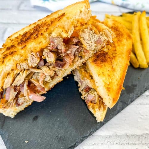 Pulled Pork Grilled Cheese Sandwich halves on a black plate with chips.