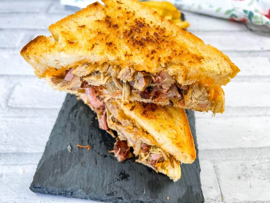 A black slate plate with a pulled pork grilled cheese sandwich.