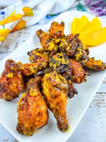 Grilled Mango-Chipotle Wings on a white platter with mango slices.