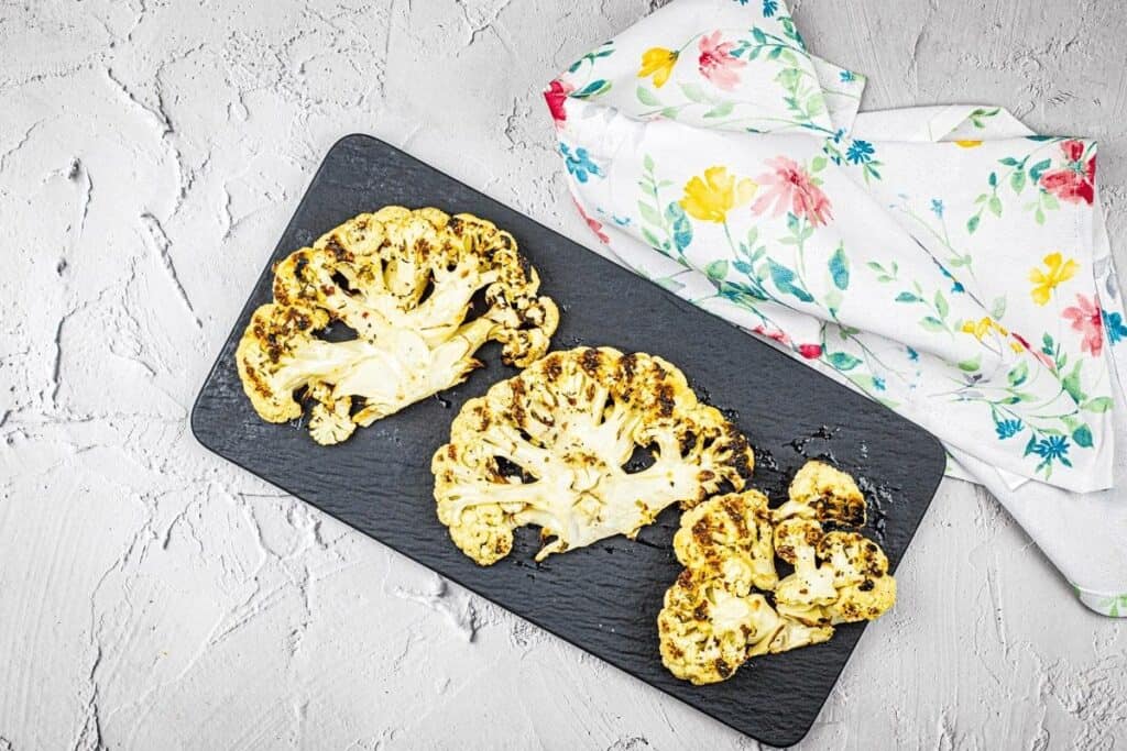 Grilled cauliflower steaks on a black plate.
