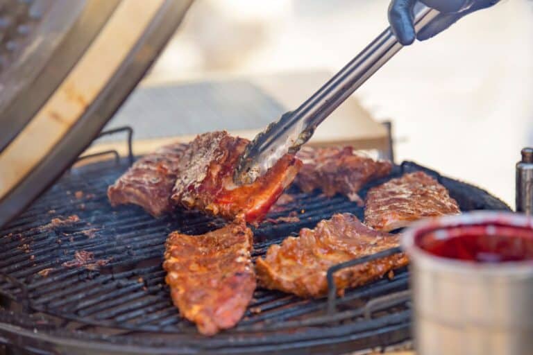 A man turns a piece of grilled ribs with tongs while grilling meat.