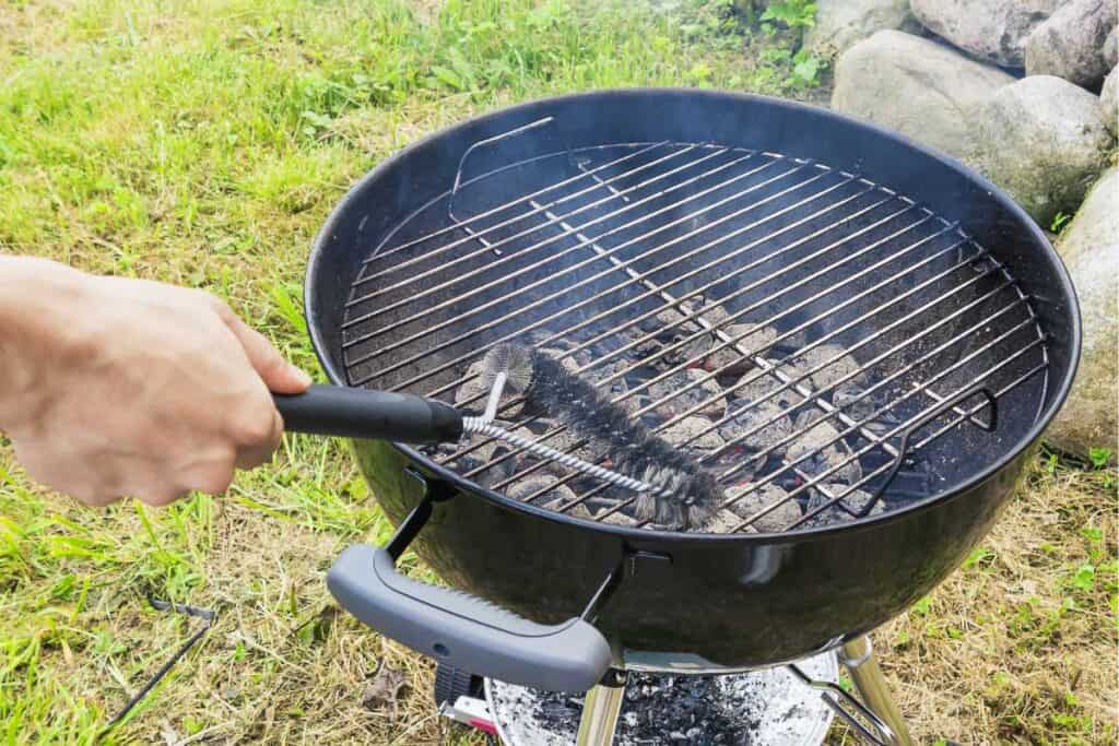Male-hand-cleans-stiff-brush-round-grill-before-cooking.