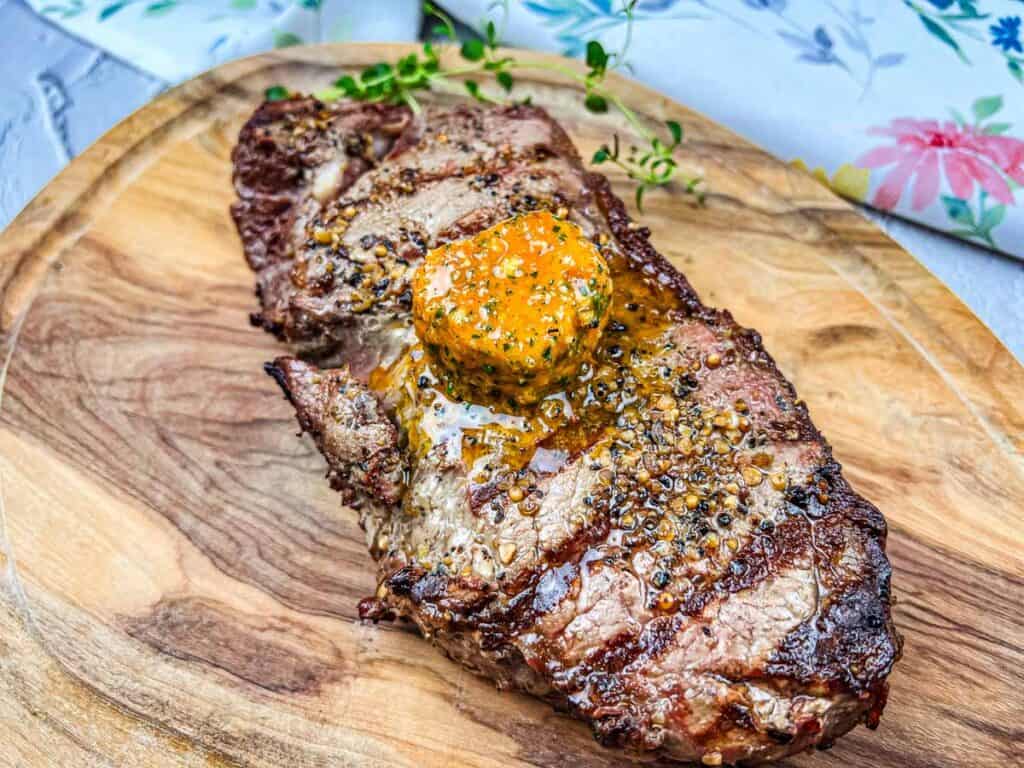 Grilled steak with cowboy butter on a cutting board.