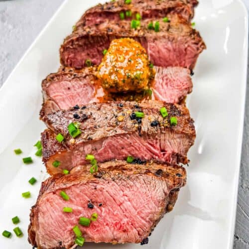 Sliced steak on a white plate with cowboy butter.