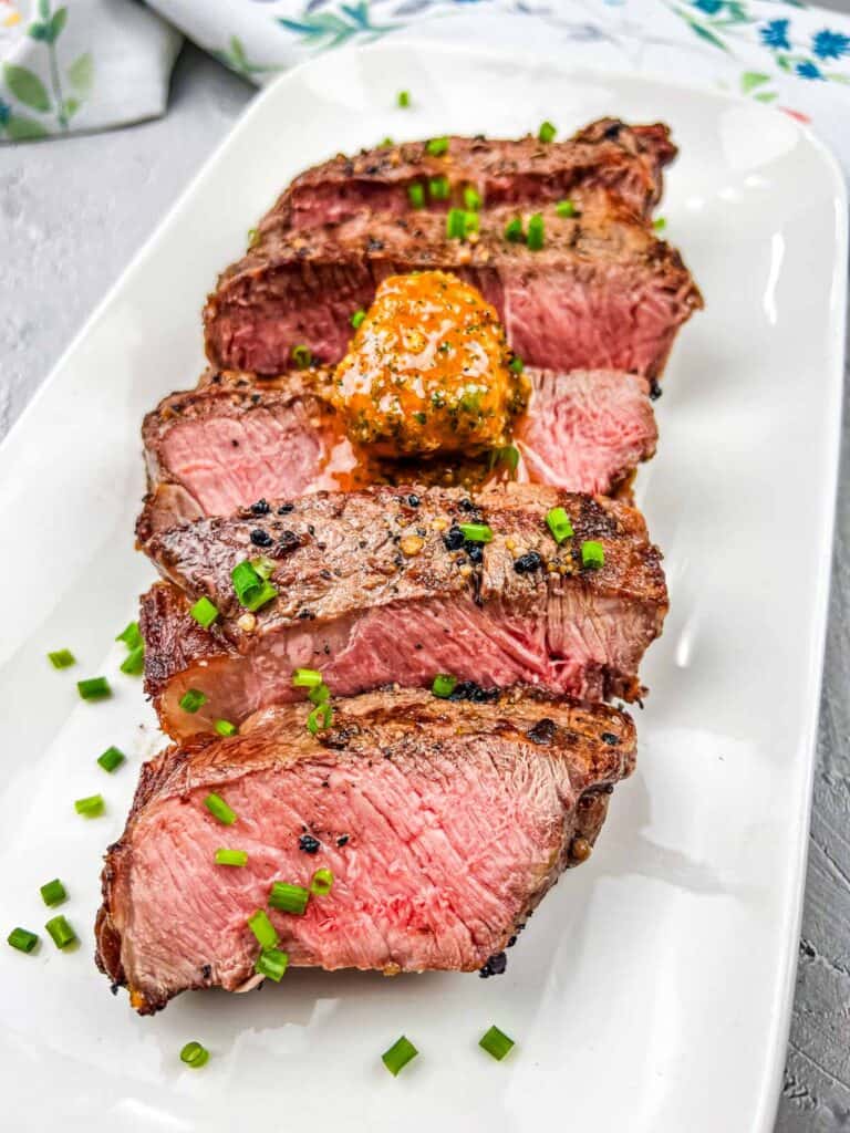 Sliced steak on a white plate with cowboy butter.