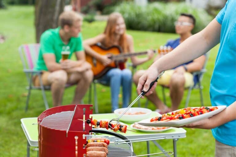 Man grilling on a BBQ with friends in the bckground.