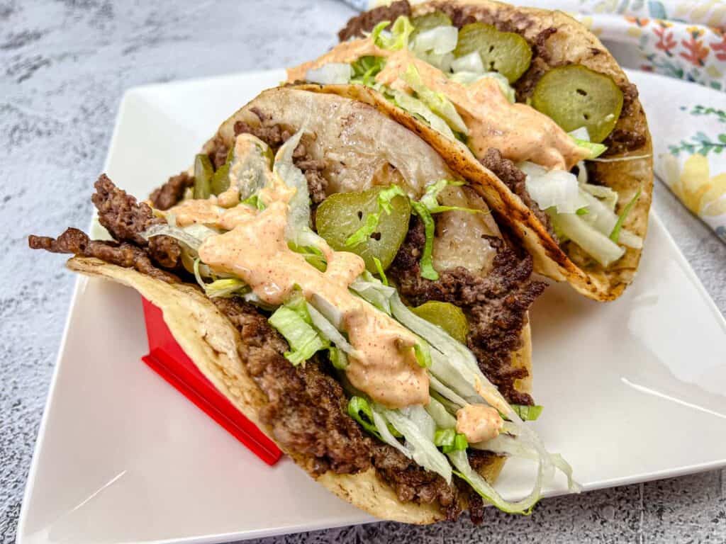 A plate of Two pieces of Blackstone Griddle Big Mac Tacos with a sauce drizzled on top.