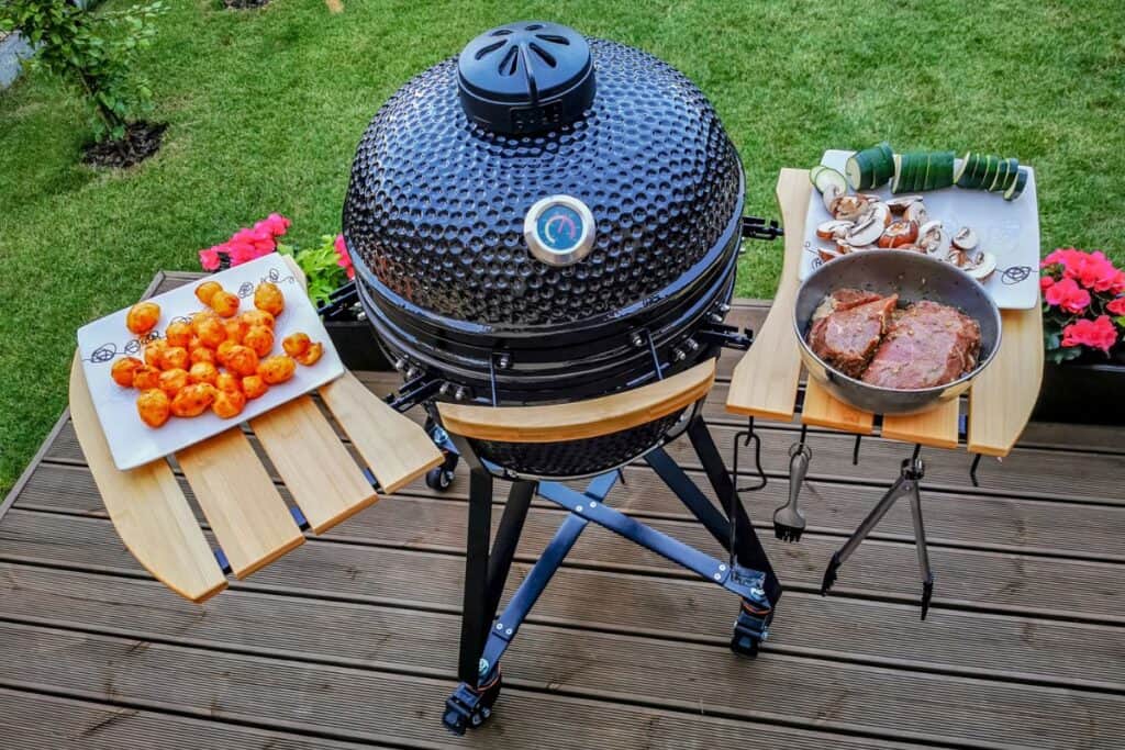 Large kamado type barbeque grill with beef steaks and vegetables ready to cook.