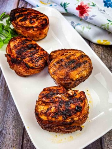 A Ninja Woodfire Grill Bacon-Wrapped Chicken Breasts served on a white rectangular plate.