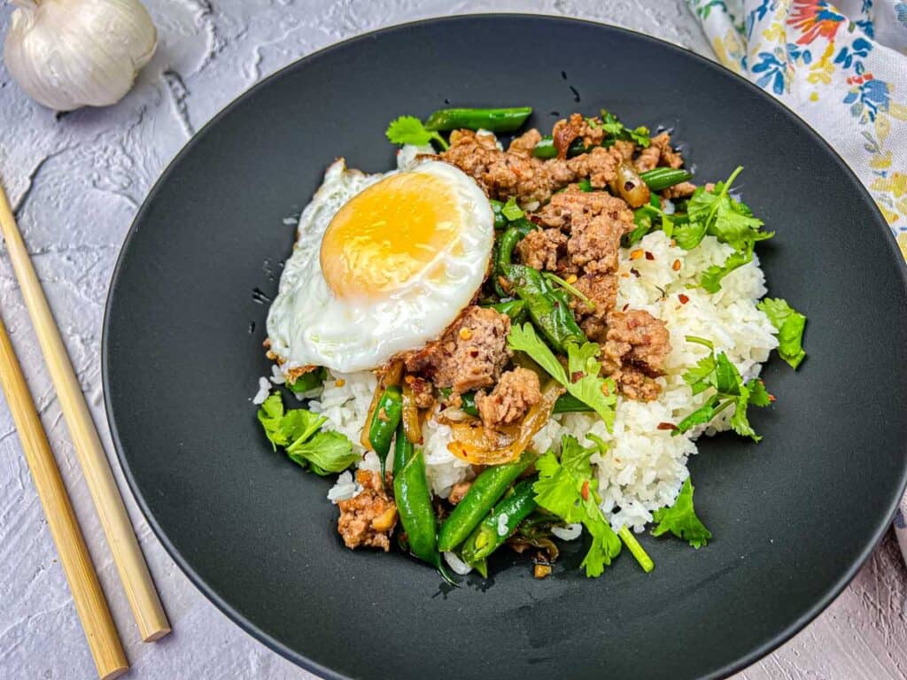 A plate of Sizzling Thai Pork & Green Beans with egg on top.