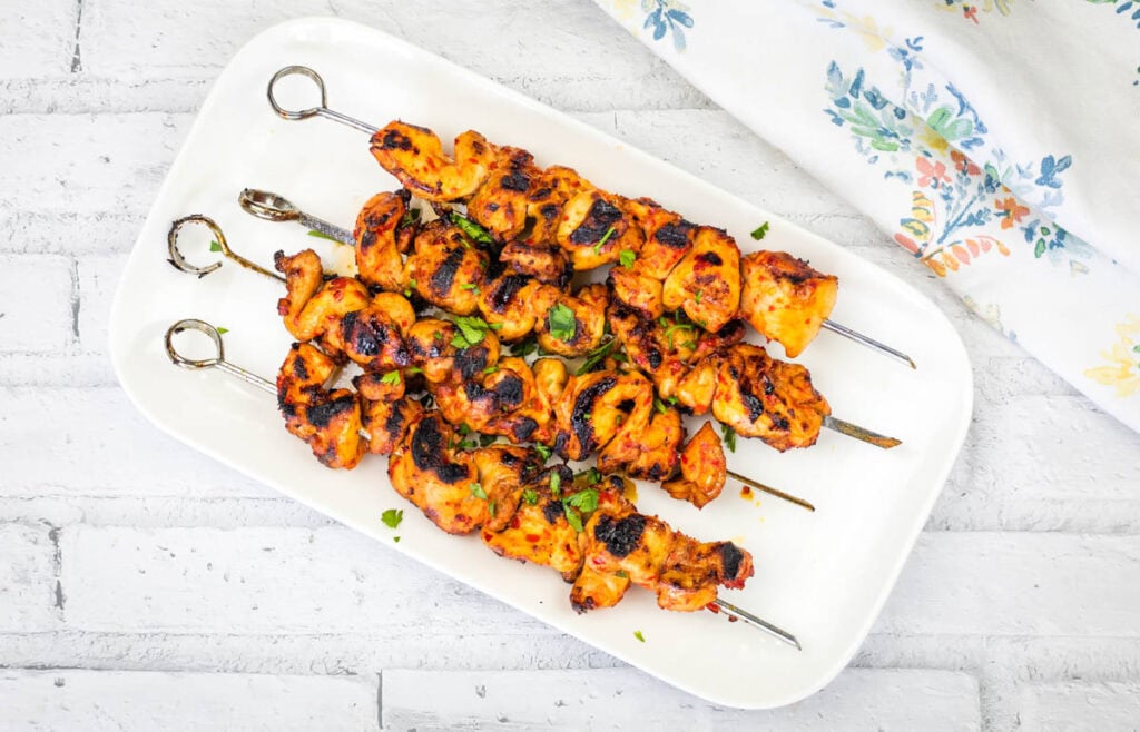 Top-down shot of Grilled Harissa-Honey Chicken Skewers served on a white rectangular plate.