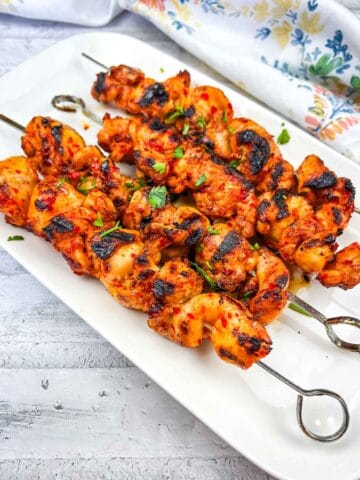 Grilled Harissa-Honey Chicken Skewers on a white rectangular plate.