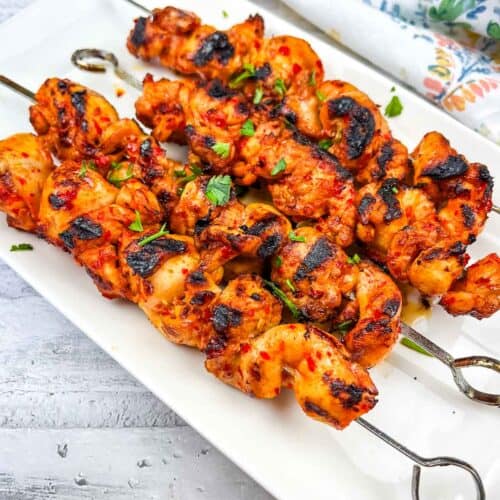 Grilled Harissa-Honey Chicken Skewers on a white rectangular plate.