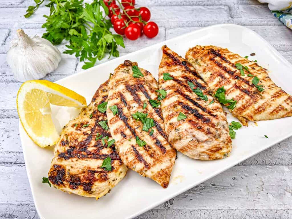 Four pieces of Ninja Woodfire Grill Lemon-Herb Chicken on a white plate.