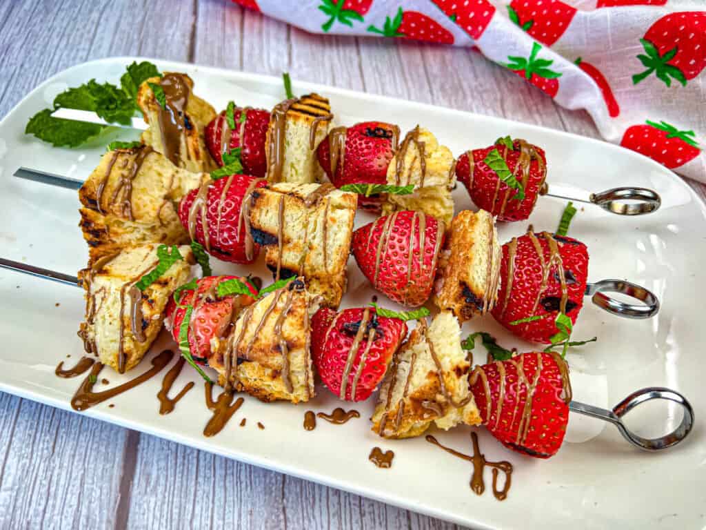 Three pieces of a Grilled Strawberry Shortcake Skewers on a white plate.