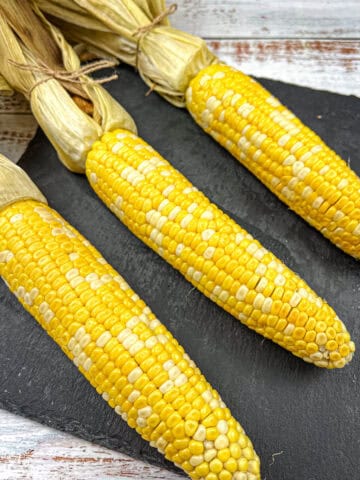 Smoked corn on the cob on a black slate plate.