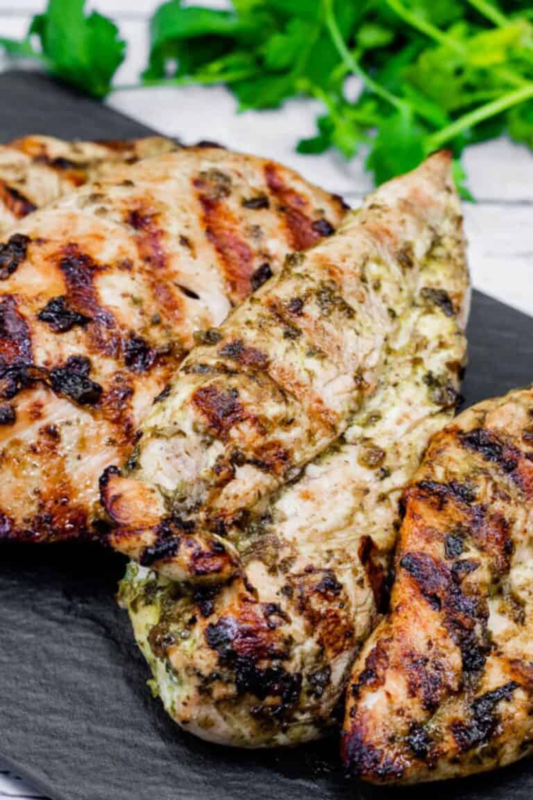 A close-up grilled chicken on a black stone-like board with cilantro leaves in the background.