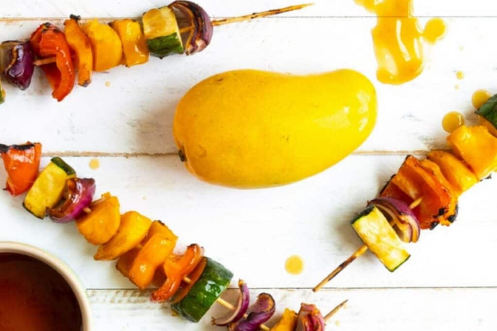 Three pieces of Grilled teriyaki mango skewers with teriyaki sauce and mango on a white wooden table.