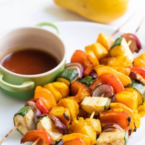 Four pieces of Grilled teriyaki mango skewers with teriyaki sauce on a white plate.
