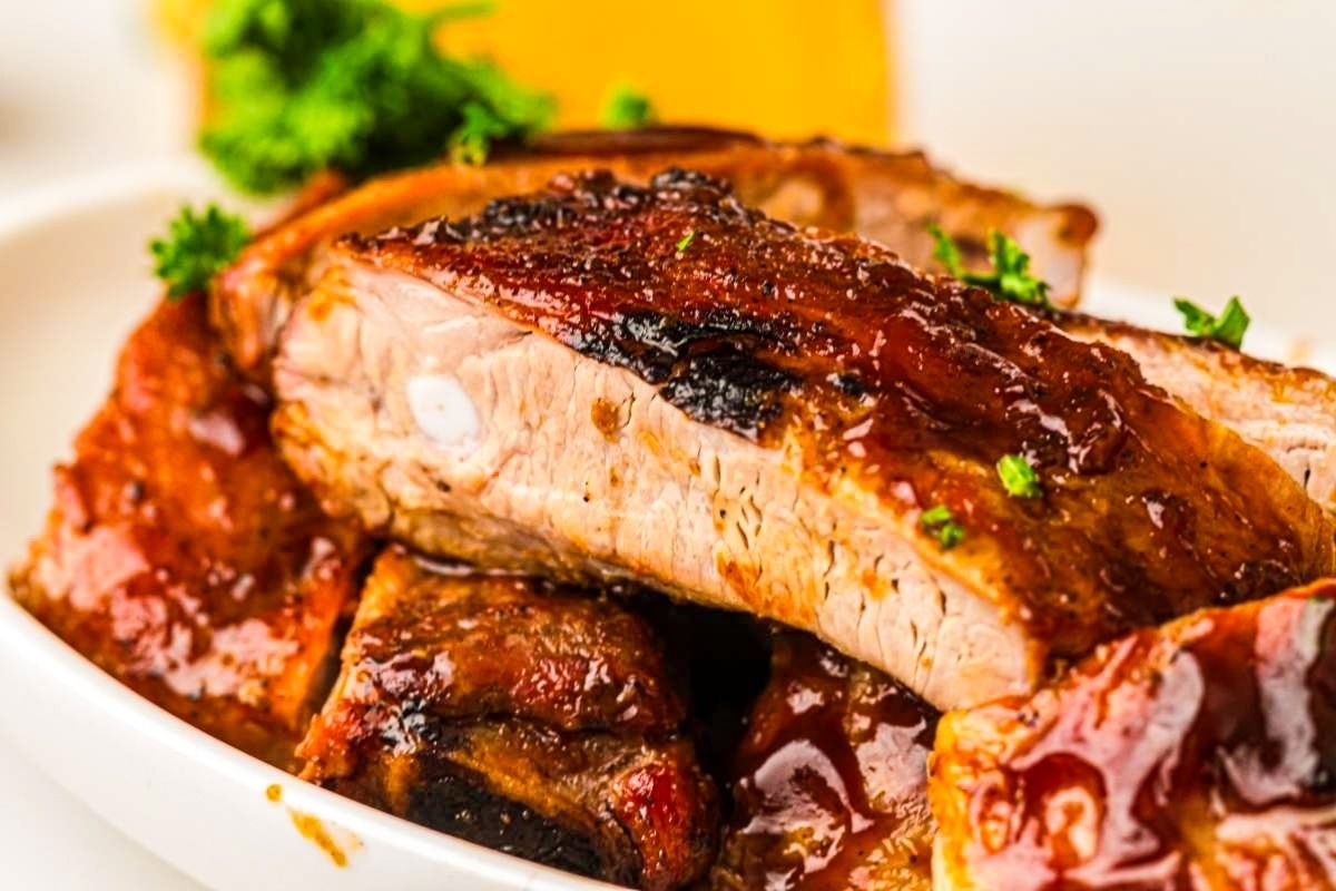 A close-up shot of grilled ribs placed underneath another cut of ribs on a plate.