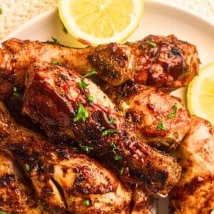 A plate of pieces of grilled chicken drumsticks topped with chopped parsley beside a lemon.