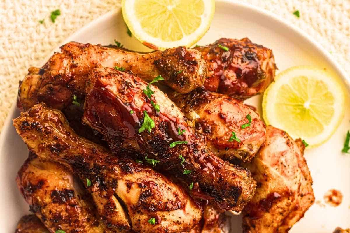 A plate of pieces of grilled chicken drumsticks topped with chopped parsley beside a lemon.