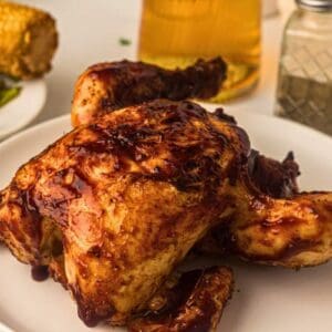 Grilled whole chicken glazed with BBQ sauce on a plate.