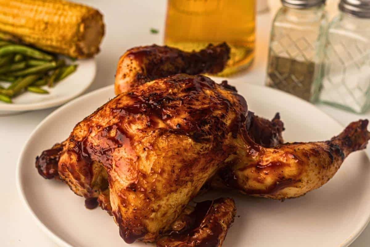 Grilled whole chicken glazed with BBQ sauce on a plate.