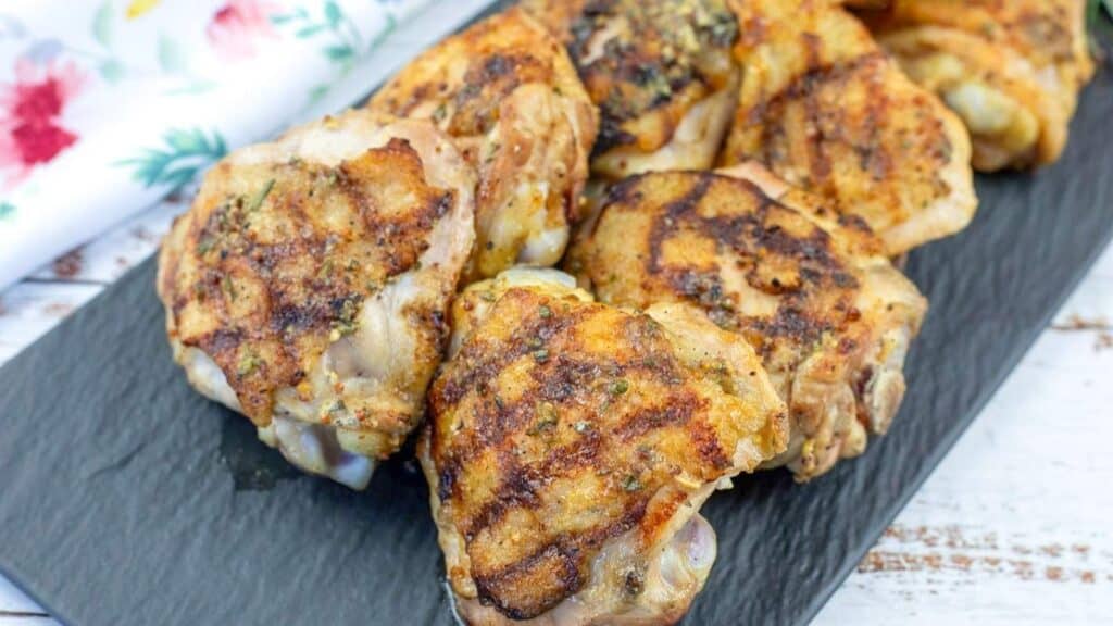 Close-up pieces of Grilled Dijon Rosemary Chicken Thigh on a slate plate.