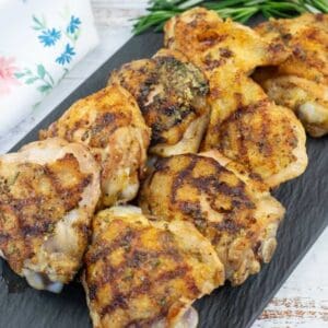 A piece of grilled Dijon rosemary chicken thighs served on a black slate plate.