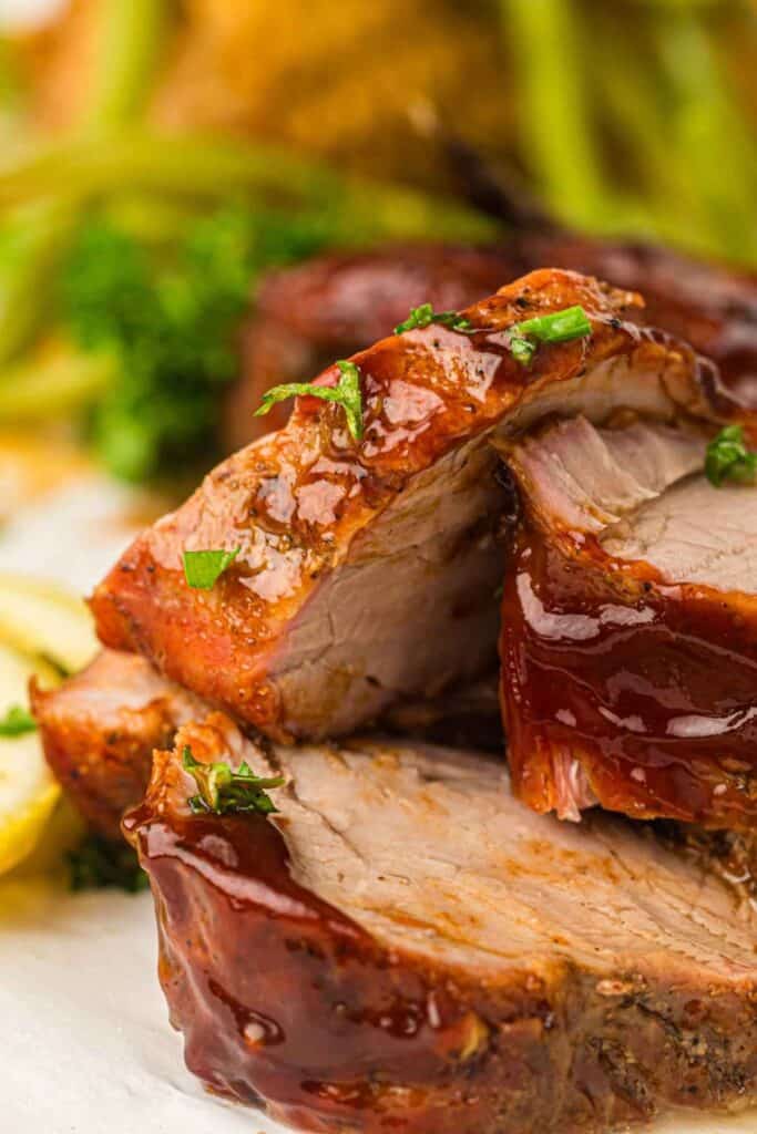 Pieces of Grilled Pork Tenderloin garnished with herbs on a white plate.